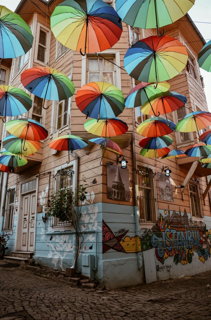 Vibrant umbrellas float above a graffitied street in Istanbul, creating a colorful canopy.