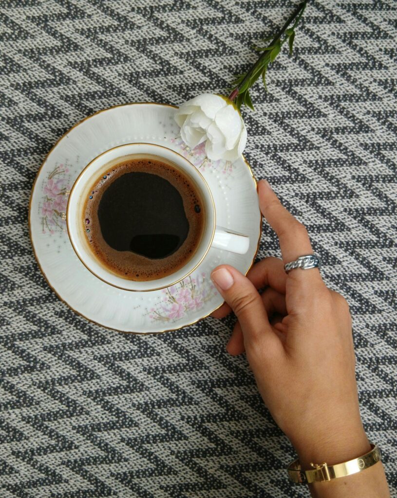 A hand reaches for a cup of coffee on a textured surface with a white flower. Modern and serene.