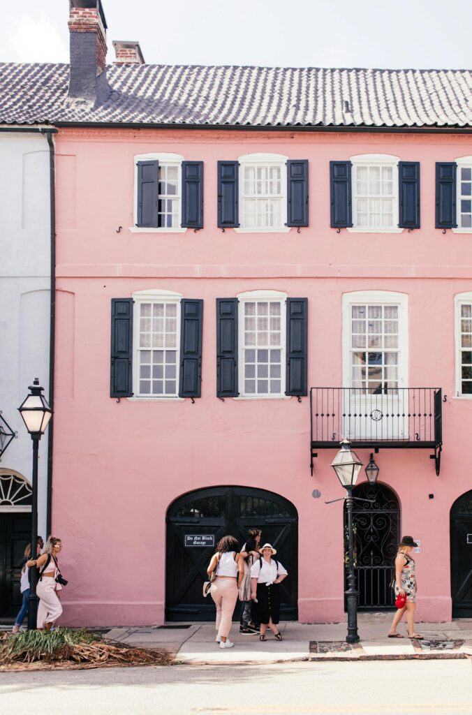 Group walking by a charming pink building in Charleston's historic district. Iconic and colorful street view.