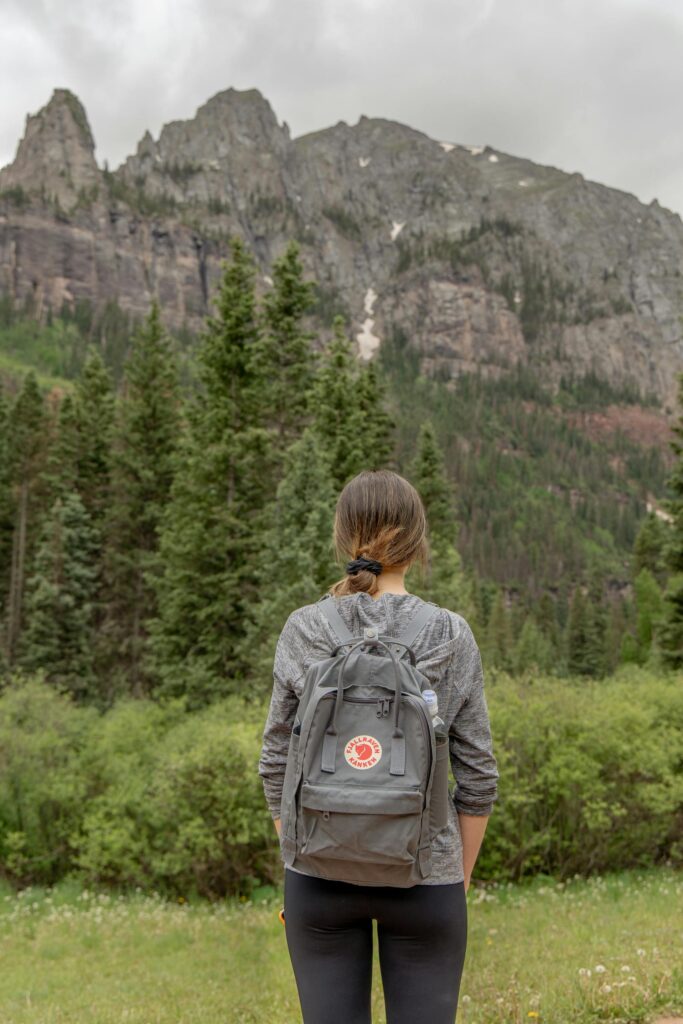 Woman hiking with backpack in Telluride, CO mountains under overcast sky.